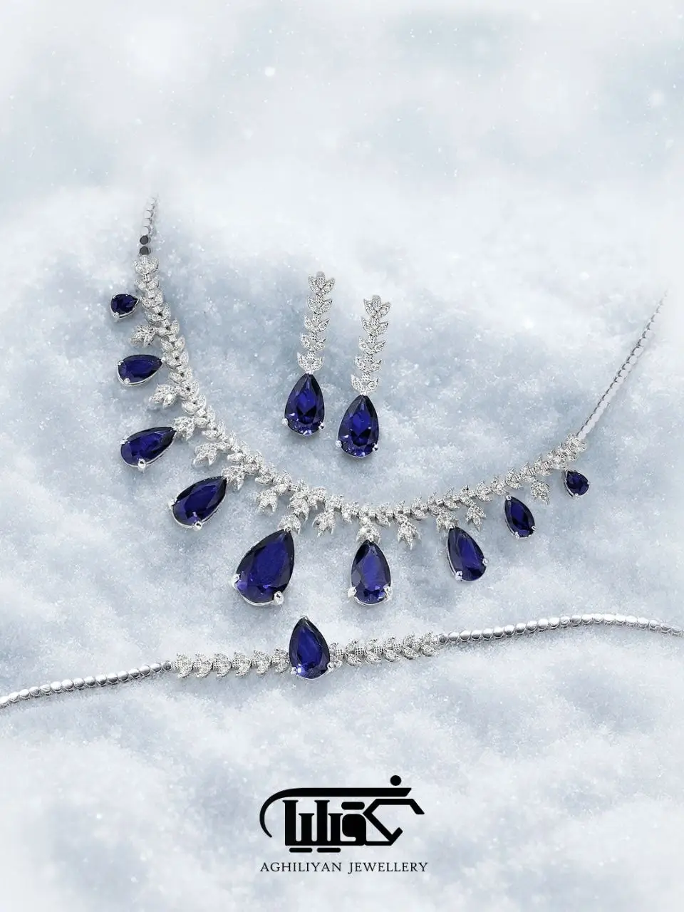 pear-cut-sapphire-suite-4120 سرویس اشک یاقوت کبود 4120 طرح برگ با سنگهای یاقوت کبود تراش اشک و الماس برلیان شامل گردنبند، گوشواره و دستبند روی زمینه برفی